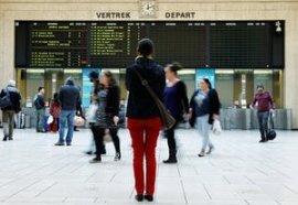 A traveller stands in front of an information board at a Belgian railway station.